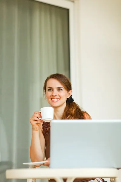Dreaming young woman sitting on terrace with laptop and cup of c — Stock Photo, Image