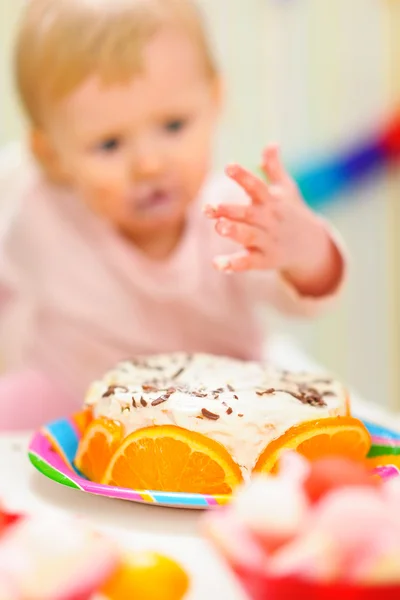 Closeup on birthday cake and eat smeared baby in background — Stock Photo, Image