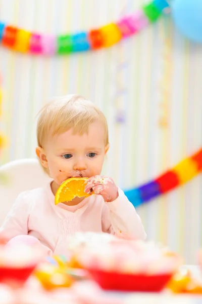 Baby eating orange on first birthday celebration party — Stock Photo, Image