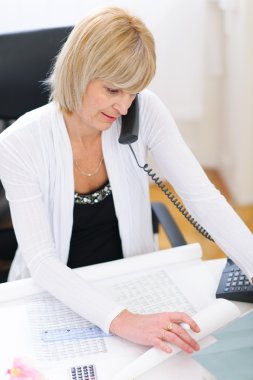 Senior architect woman speaking phone and looking on blueprints clipart