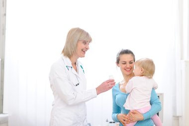 Senior pediatric doctor giving pills bottle to mother with baby clipart