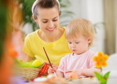 Mom helping baby painting on Easter eggs clipart