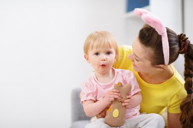 Baby sitting on mother lap and enjoying Easter rabbit cookie clipart