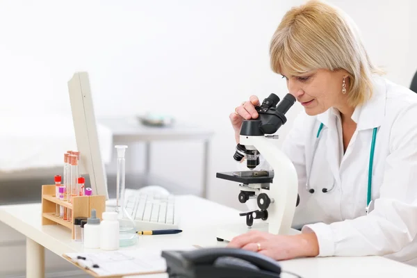 Médica sênior olhando em microscópio no laboratório — Fotografia de Stock