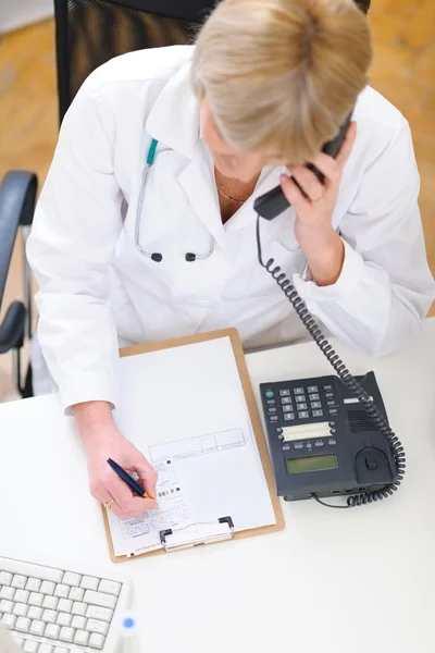 Doctor woman speaking phone and making notes in clipboard — Stock Photo, Image