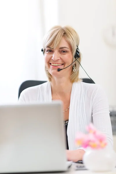 Χαμογελώντας γυναίκα ανώτερα των επιχειρήσεων με το ακουστικό που εργάζονται στο lap-top — Φωτογραφία Αρχείου