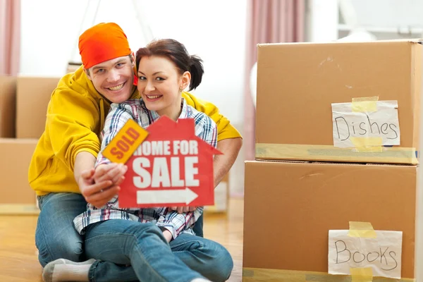 Hugging young couple showing home for sale sign with sold sticke — Stock Photo, Image