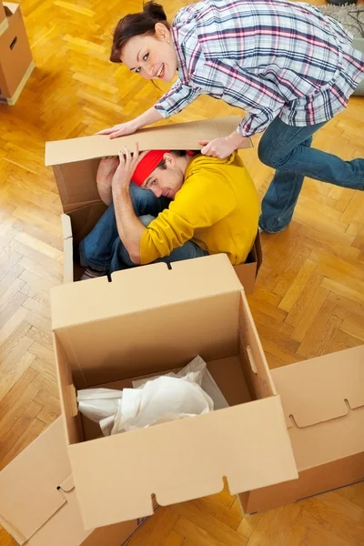 Souriante fille essayant d'emballer petit ami dans une boîte en carton — Photo