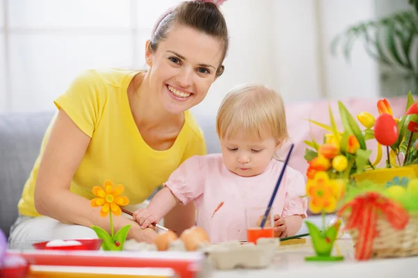 Счастливая мать помогает ребенку рисовать на пасхальных яйцах — стоковое фото