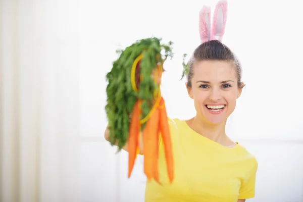Femme souriante aux oreilles de lapin montrant un tas de carottes — Photo