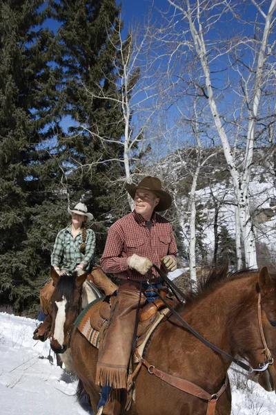 Homme et femme chevauchant des chevaux dans la neige — Photo