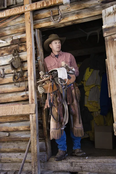 Homem vestindo chapéu de vaqueiro segurando uma sela — Fotografia de Stock