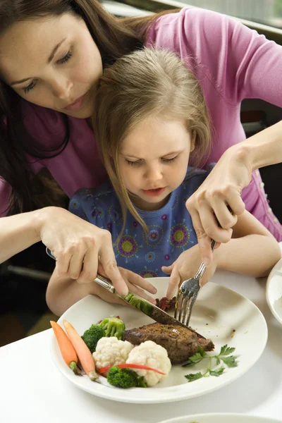 Mom helping daughter cut food. — Stockfoto