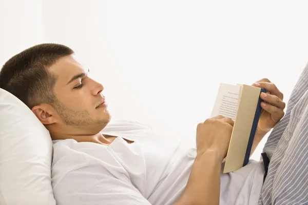 Człowiek czytania książki w łóżku. — Zdjęcie stockowe
