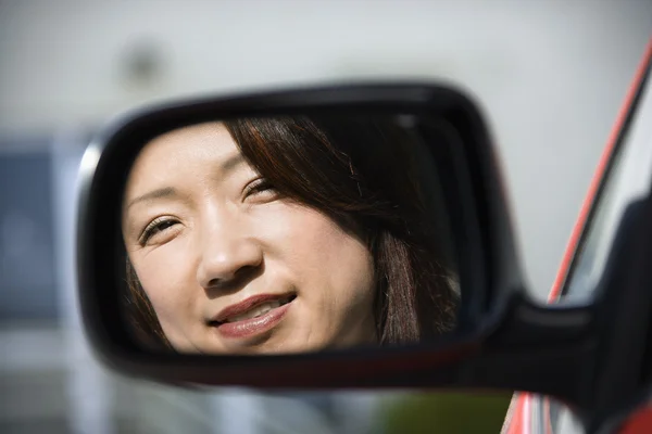 Mujer sonriente en el espejo del coche — Foto de Stock