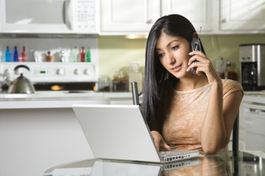 Young Woman Using Laptop and Talking on Cellphone clipart