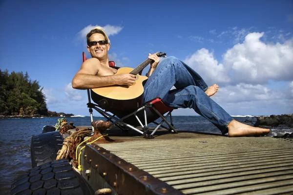 Молодой человек сидит на берегу озера и играет на гитаре — стоковое фото