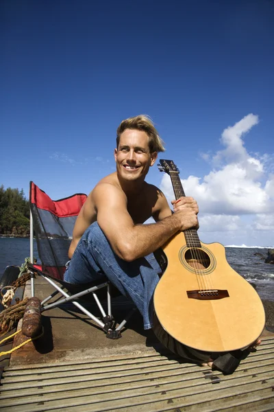 Fiatalember ült tóparti gazdaság gitár — Stock Fotó