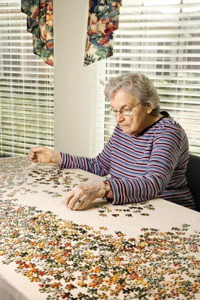 Oudere vrouw doet jig saw puzzel — Stockfoto