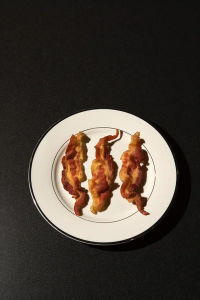 Três tiras de bacon cozido na placa branca — Fotografia de Stock
