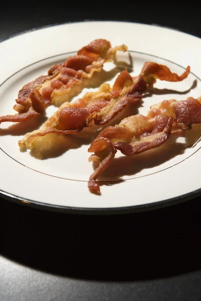 Trois bandes de bacon cuit sur plaque blanche — Photo