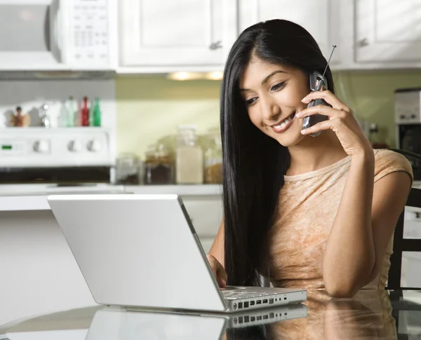 Jovem mulher usando laptop e conversando no celular — Fotografia de Stock