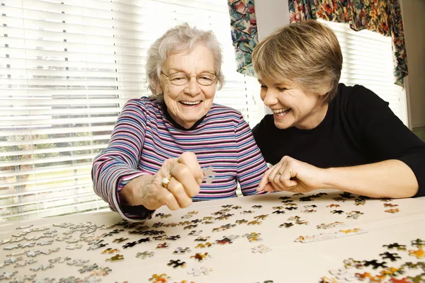 高齢者の女性と若い女性のパズルをやっています。 ストック写真