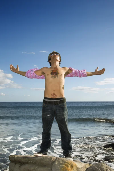 Junger Mann steht mit ausgestreckten Armen auf Meeresfelsen — Stockfoto