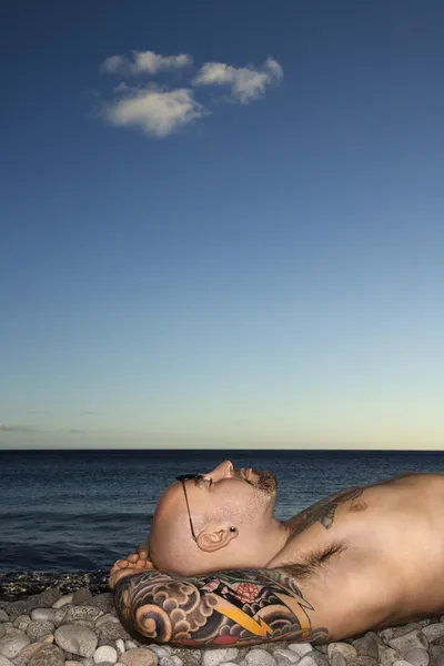 纹身的男子躺在海滩上 — 图库照片