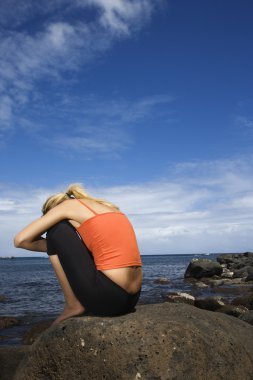 Woman sitting on rocky shore. clipart