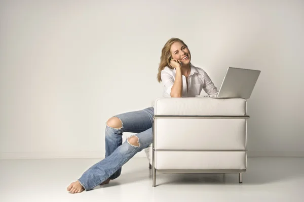 Mujer joven sentada en silla con un ordenador portátil y teléfono celular —  Fotos de Stock