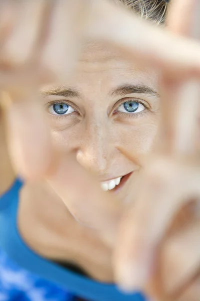 Woman smiling through framed fingers. — Stock Photo, Image