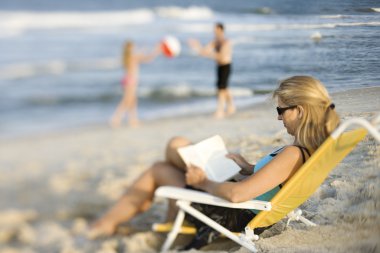 Mom reading book on beach. clipart