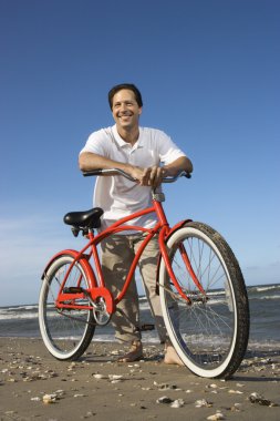 Man leaning on bike at beach. clipart