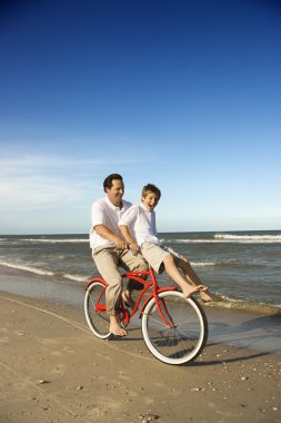 Dad riding red bicycle with son on handlebars. clipart