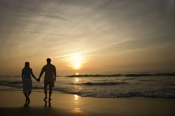 Paar spaziert bei Sonnenuntergang am Strand — Stockfoto