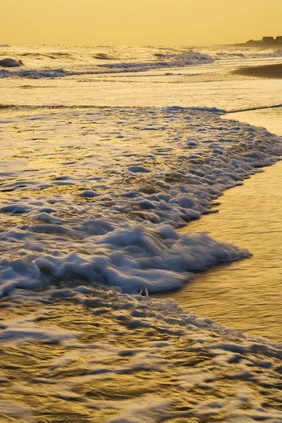 Хвилі пливуть пляж на заході сонця . — стокове фото