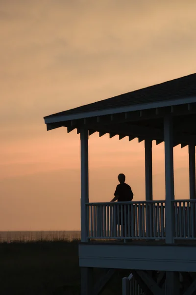 Chłopiec na werandzie przy plaży o zachodzie słońca — Zdjęcie stockowe