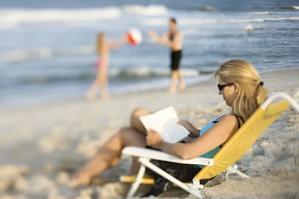 Mom reading book on beach. Stock Photo