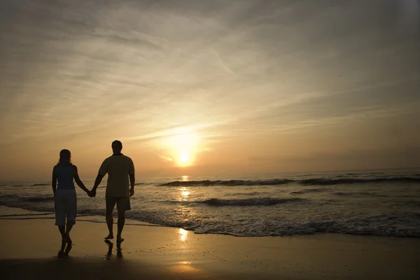 Paar spaziert bei Sonnenuntergang am Strand lizenzfreie Stockfotos