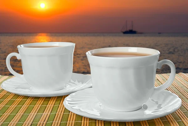 Två vita koppar med tefat på bakgrund av solnedgången. — Stockfoto