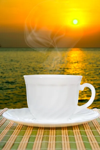 Vit kopp med fat på bakgrund av solnedgången. — Stockfoto