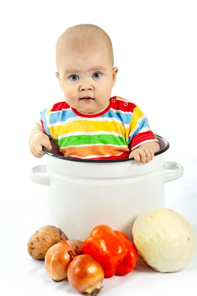 Baby sitting in the big saucepan with vegetables. — Stock Photo, Image