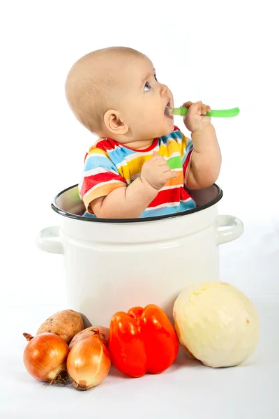 Baby sitzt im großen Topf mit Gemüse. Stockbild