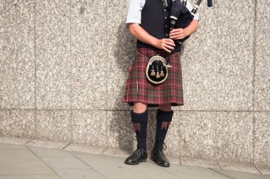 Bagpiper dressed in kilt playing bag pipes clipart