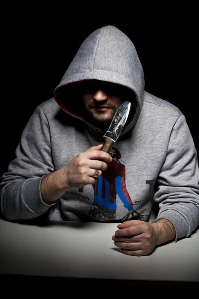 Mann in Kapuze mit Messer am Tisch Stockfoto