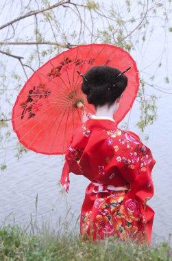 Geisha with red umbrella at the riverside clipart