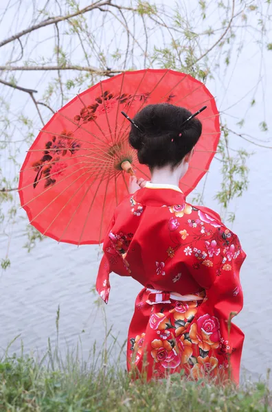 Гейша с красным зонтиком на берегу реки — стоковое фото