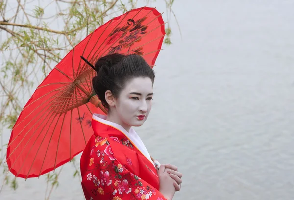 Geisha with red umbrella at the riverside — Stock Photo, Image