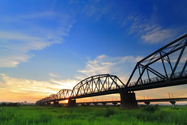 stock image Beautiful sunset with old bridge and green grass